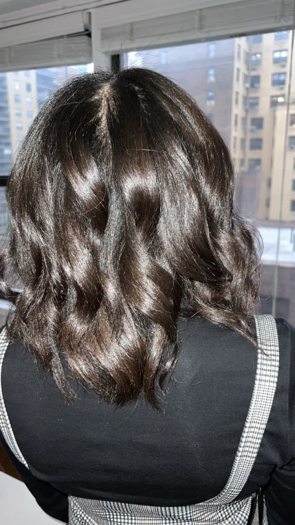 A photo showing the back of a woman's head. She has soft waves in her brown hair.