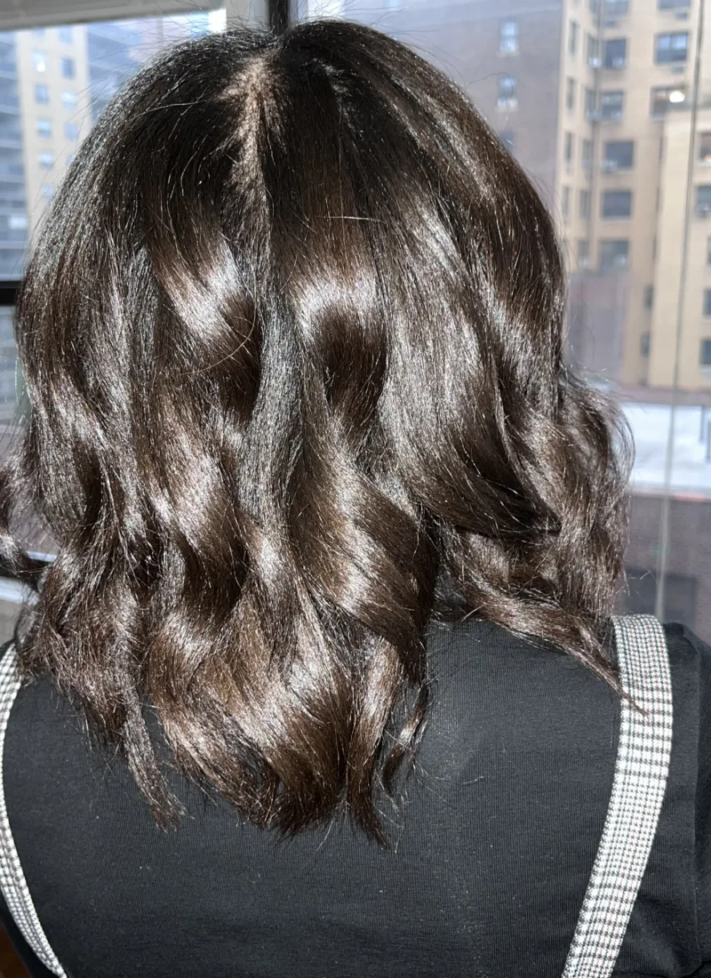 A photo showing the back of a woman's head. She has soft waves in her brown hair.