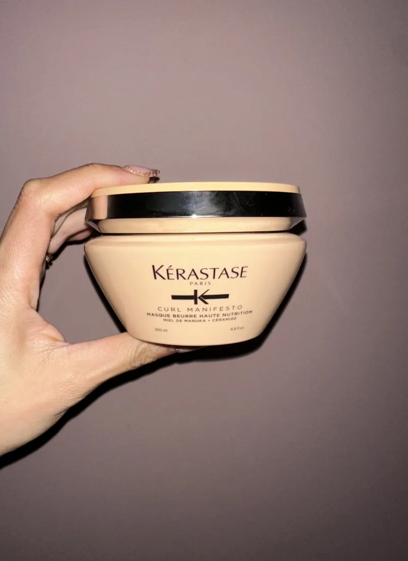 A hand holding a bottle of Kerastase Curl Manifesto Masque Beurre Haute Nutrition hair mask, a deep conditioning treatment for curly hair.