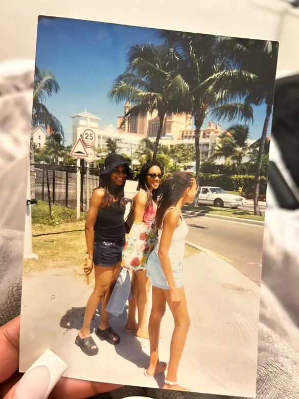 Three girls wearing braids with palm trees in the back.