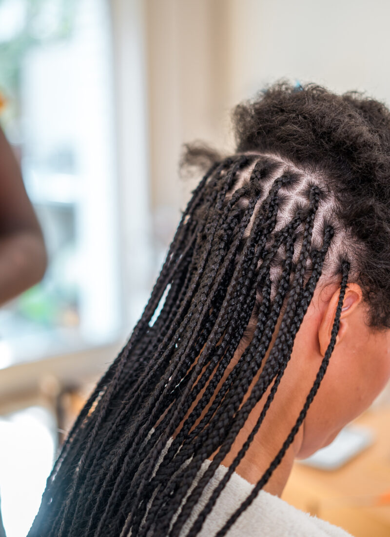 Mixed race female having her hair styled into braids by a mid adult Black female in a home setting.